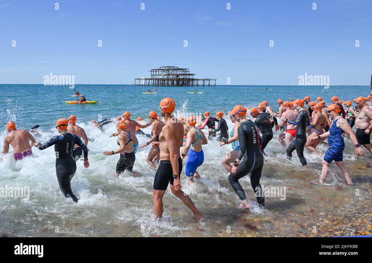 Brighton UK 16th juillet 2022 - les nageurs chargent dans la mer pour le début de la course de Brighton Pier à Pier par une chaude journée ensoleillée. Un avertissement rouge de conditions météorologiques extrêmes a été émis pour le début de la semaine prochaine car les températures devraient atteindre 40 degrés dans certaines parties de la Grande-Bretagne . : Crédit Simon Dack / Alamy Live News Banque D'Images
