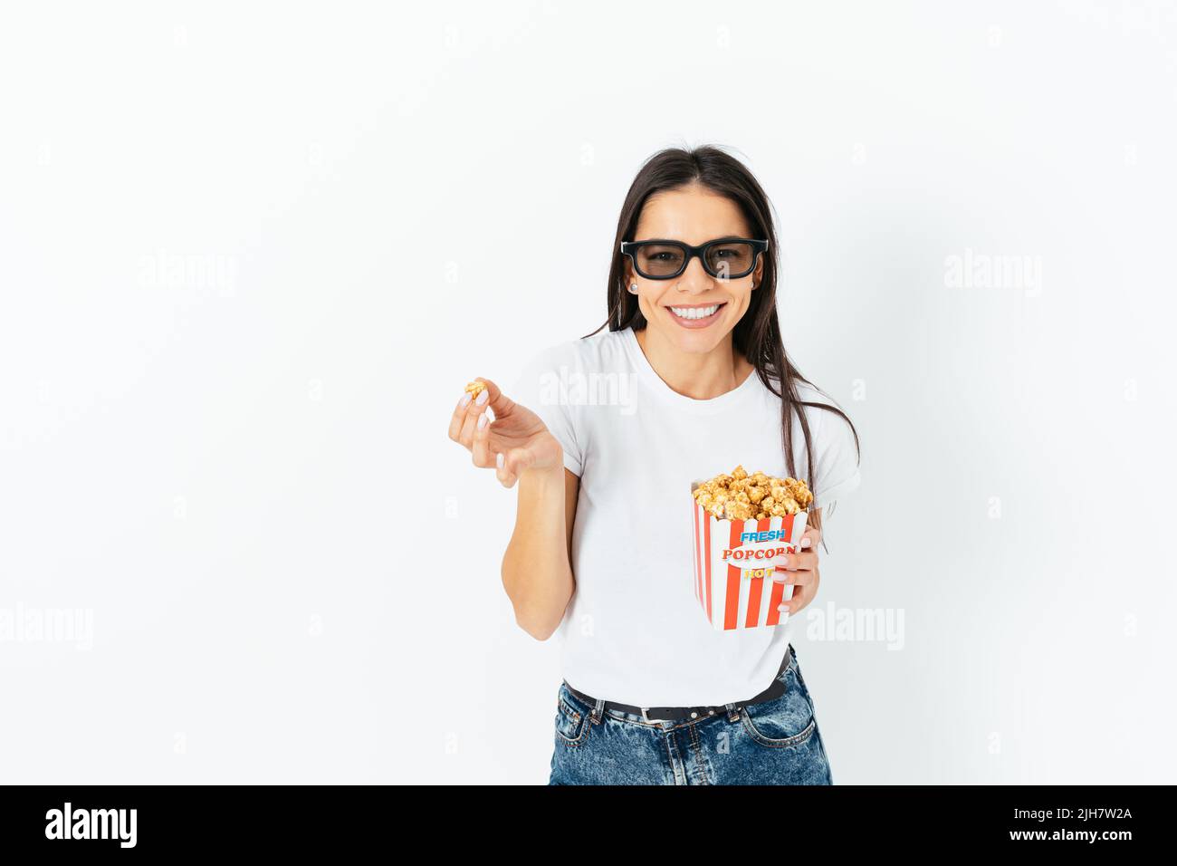 Bonne fille souriante brune dans un Jean décontracté et un t-shirt portant 3D verres manger du pop-corn, fond blanc studio Banque D'Images