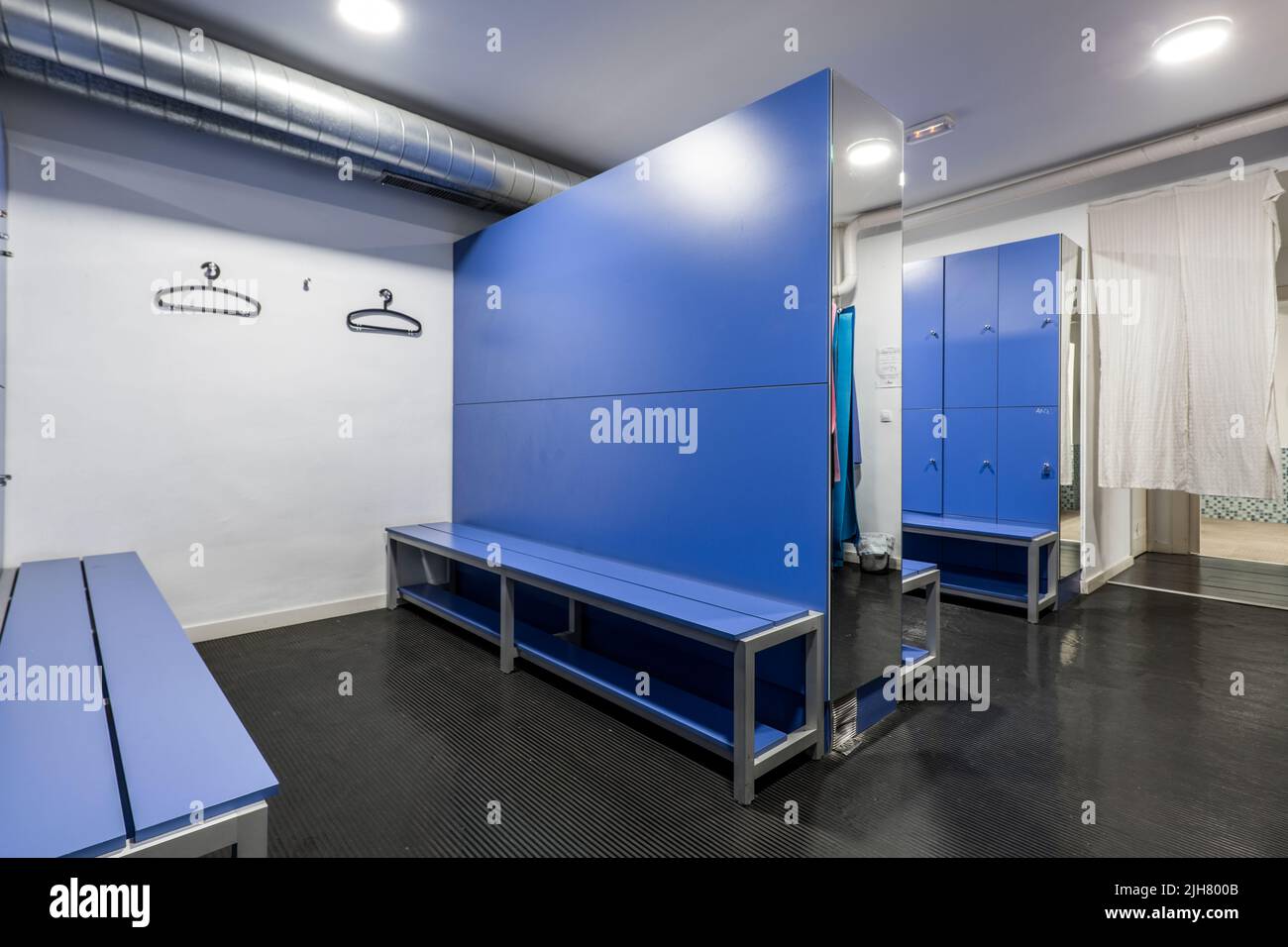 Casiers en bois bleu avec banquettes assorties, miroirs et cintres noirs dans un vestiaire de salle de gym Banque D'Images
