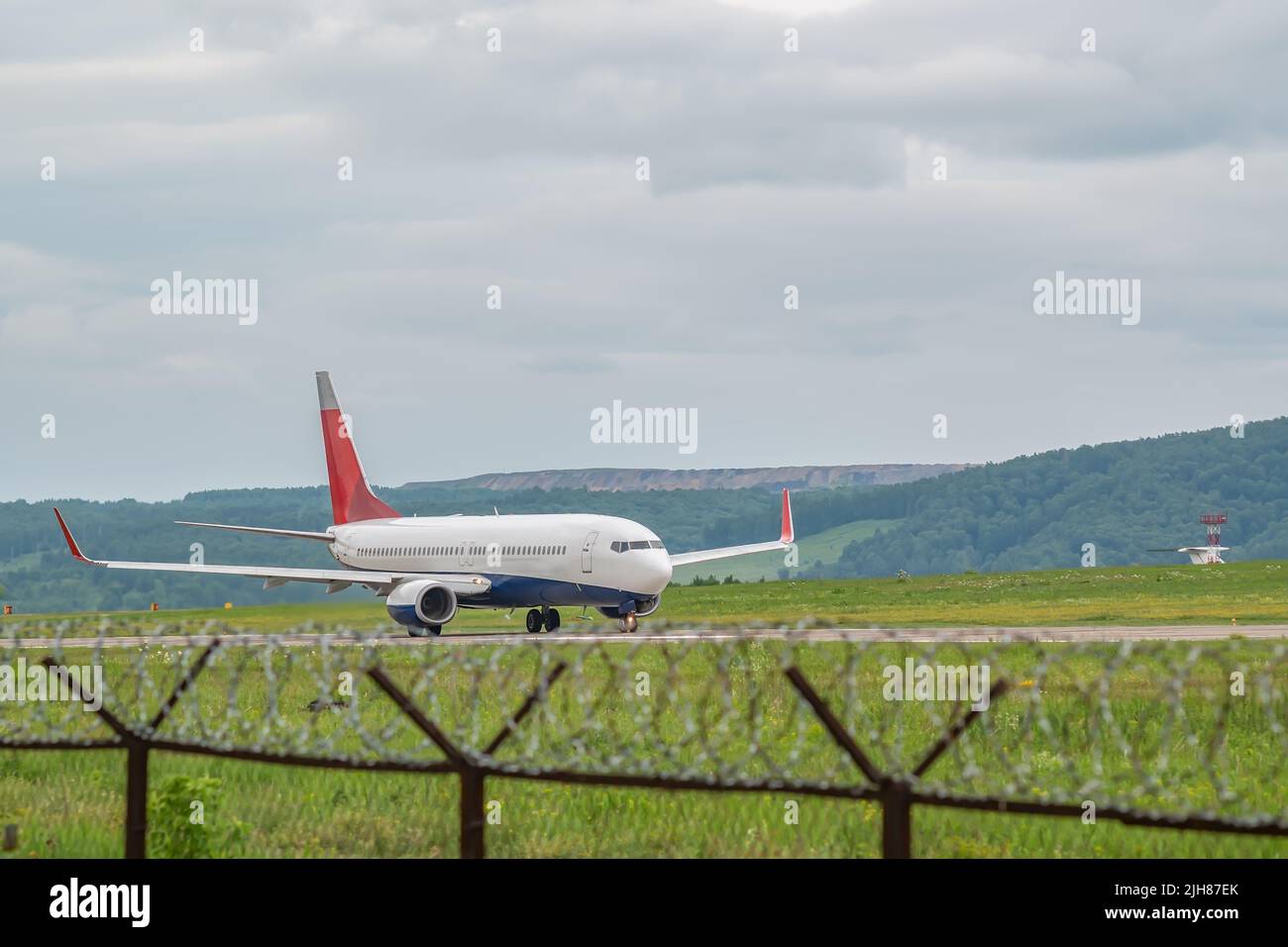 un avion de passagers civil équipé de moteurs à turbojet accélère le long de la piste sur le terrain de l'aéroport, sur fond d'une clôture barbelée Banque D'Images