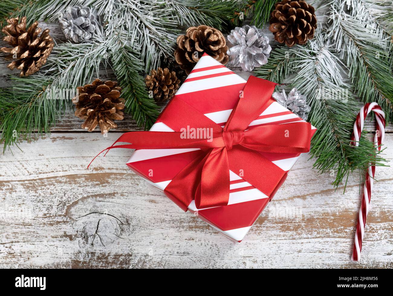 Concept de Noël et du nouvel an avec branches de sapin enneigées, boîte-cadeau traditionnelle à rayures, canne à sucre et cônes de pin argenté sur rus blanc Banque D'Images