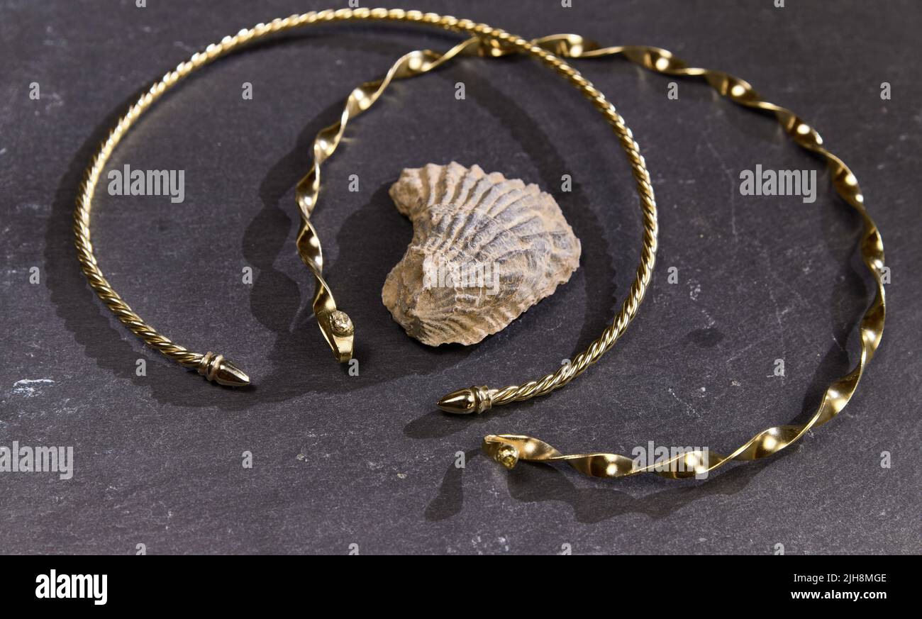 Les beaux bracelets dorés de l'époque romaine avec des motifs sur une surface noire avec ombre et un seashell Banque D'Images