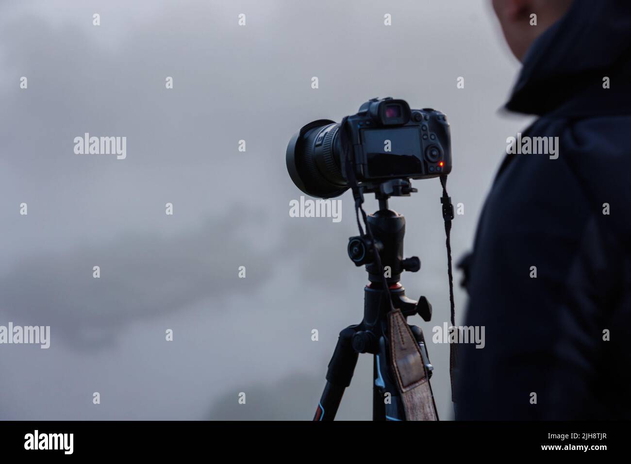 photographe méconnu qui photographie des scènes d'extérieur brumeuses avec un appareil photo numérique noir contemporain sur trépied Banque D'Images