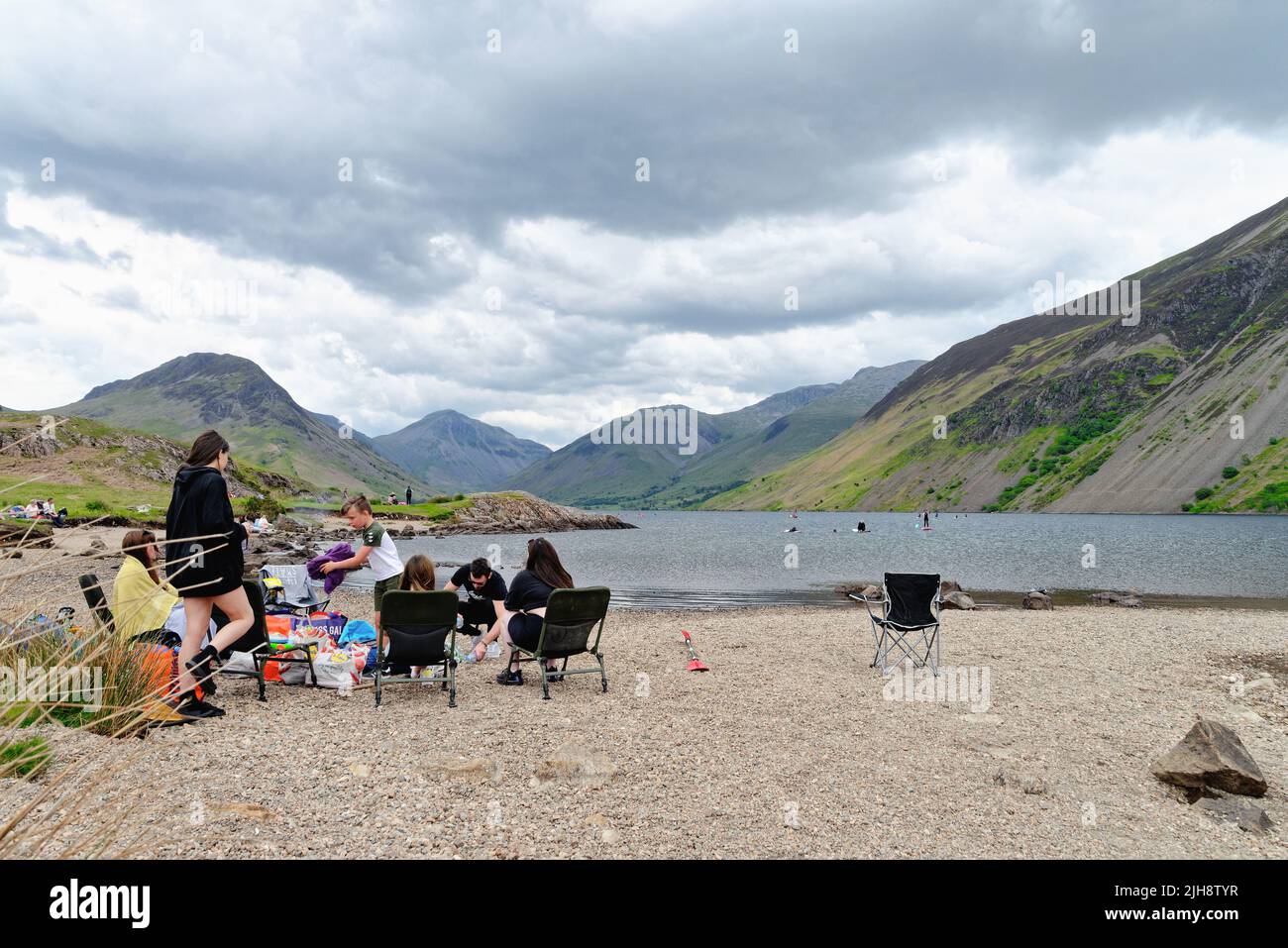 Grand groupe familial qui profite d'une journée de détente sur la plage du lac Wastwater avec le paysage de montagne spectaculaire au loin de Wasdale Cumbria Royaume-Uni Banque D'Images