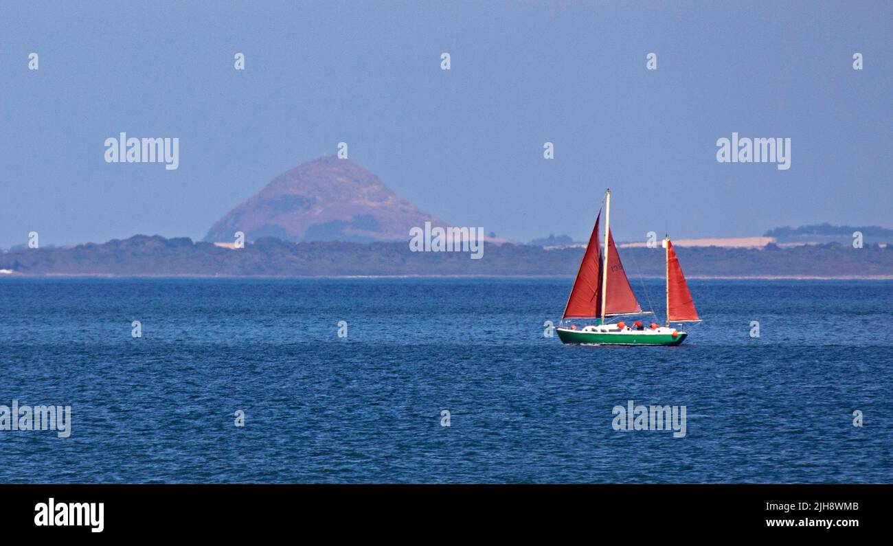 Portobello, Édimbourg, Écosse, Royaume-Uni 16th juillet 2022. Le soleil brumeux de l'après-midi s'est brisé après une matinée très nuageux, la température de 22 degrés centigrade a fait sortir un yacht à voile sur le Firth of Forth avec sa brume chaude et la loi Berwick dans le backgound. Banque D'Images