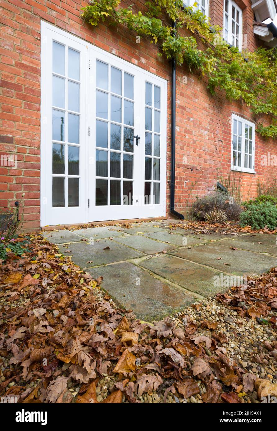 Jardin paysager britannique en automne avec feuilles, portes-fenêtres en bois et patio en pierre de York Banque D'Images