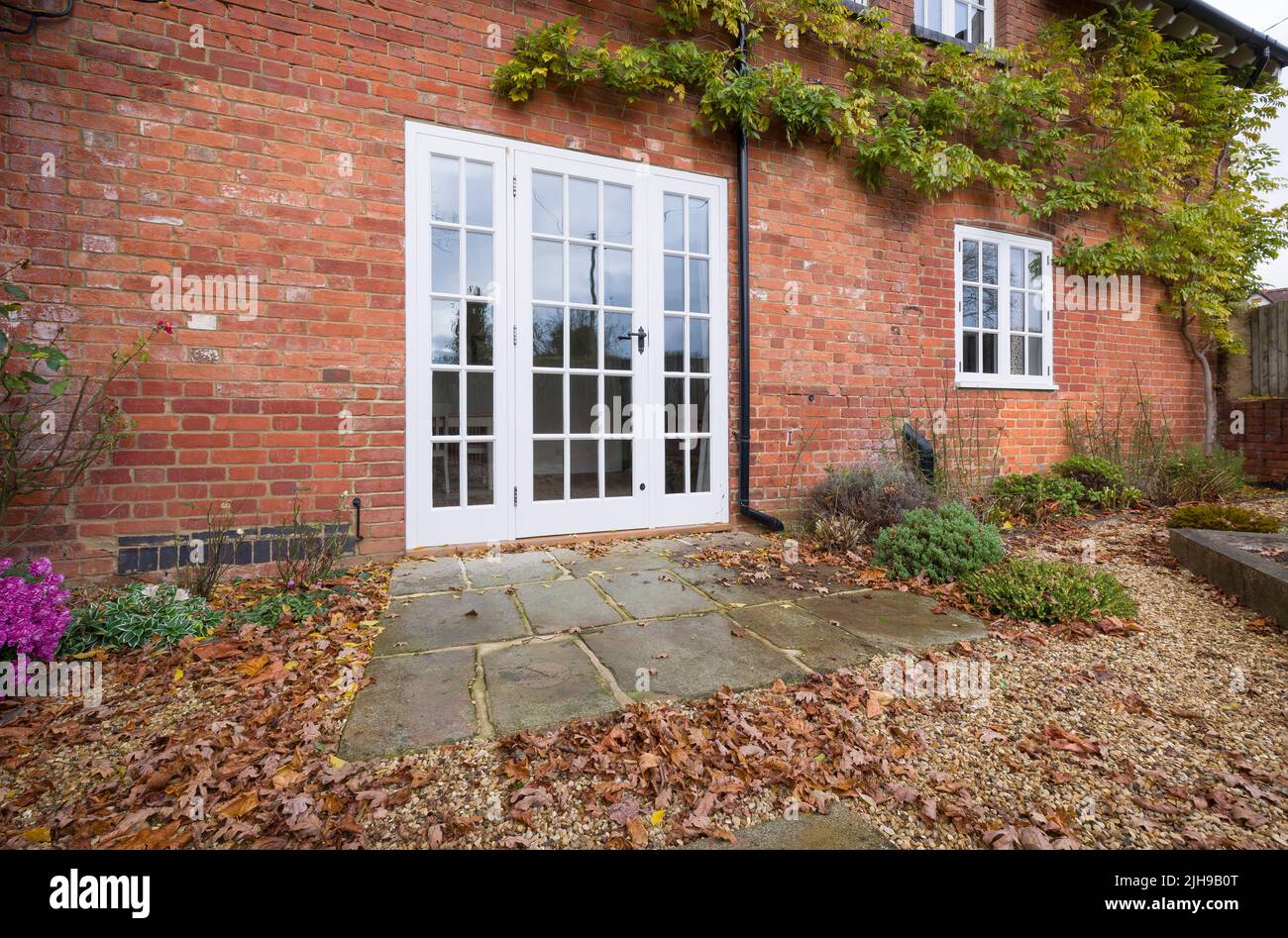 Portes-fenêtres en bois et patio en pierre de York dans un jardin paysager britannique avec feuilles d'automne Banque D'Images