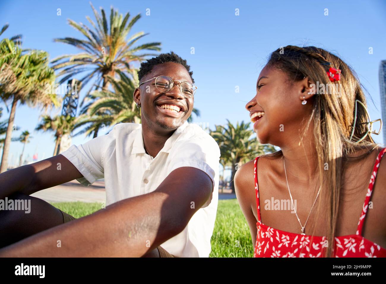 Joyeux jeune couple africain rire et s'amuser à leur première date dans le parc dans une scène romantique d'amoureux de plein air, assis sur l'herbe parlant Banque D'Images