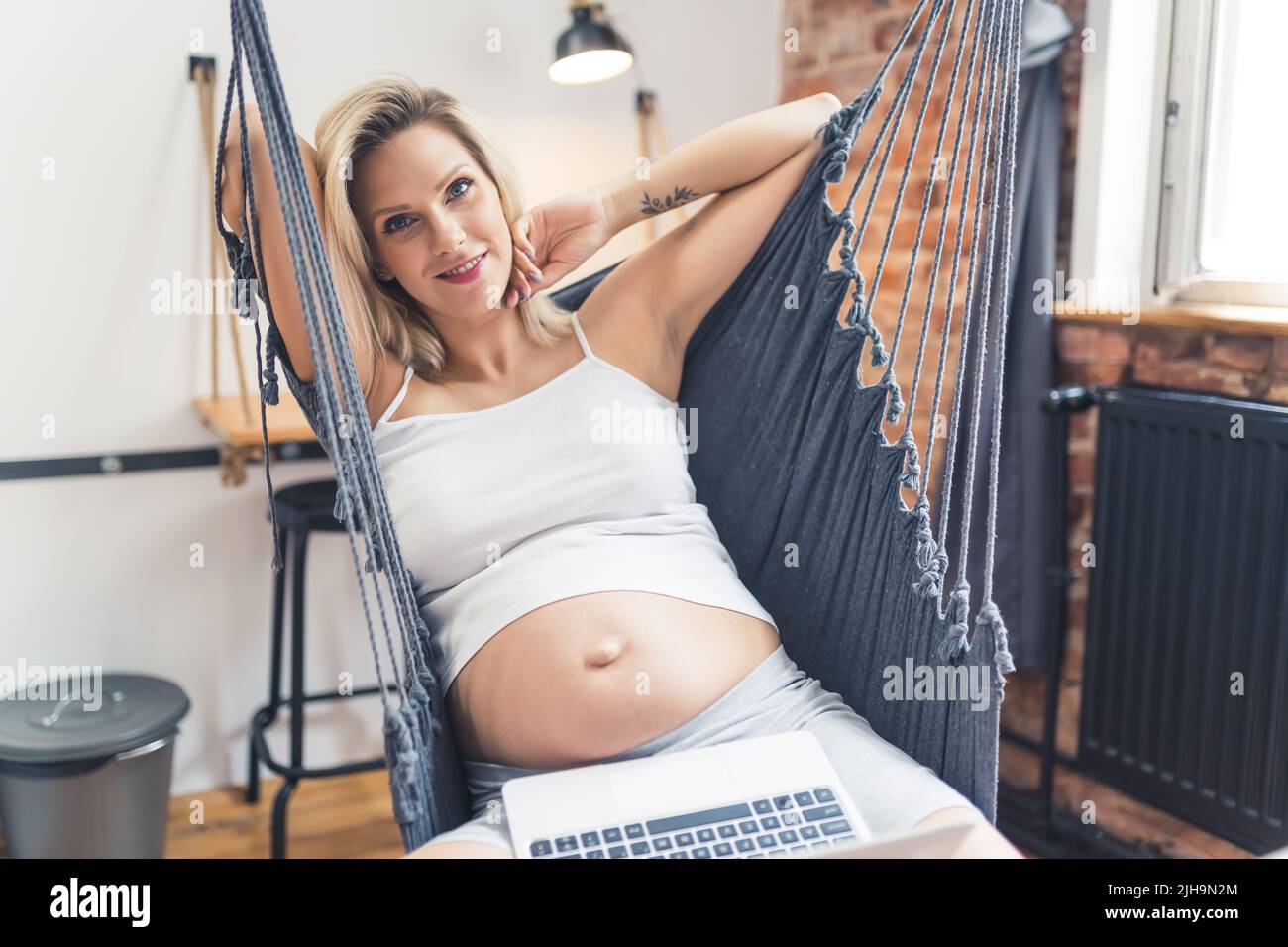 belle femme enceinte avec un ordinateur portable se relaxant dans le hamac à la maison, photo moyenne. Photo de haute qualité Banque D'Images