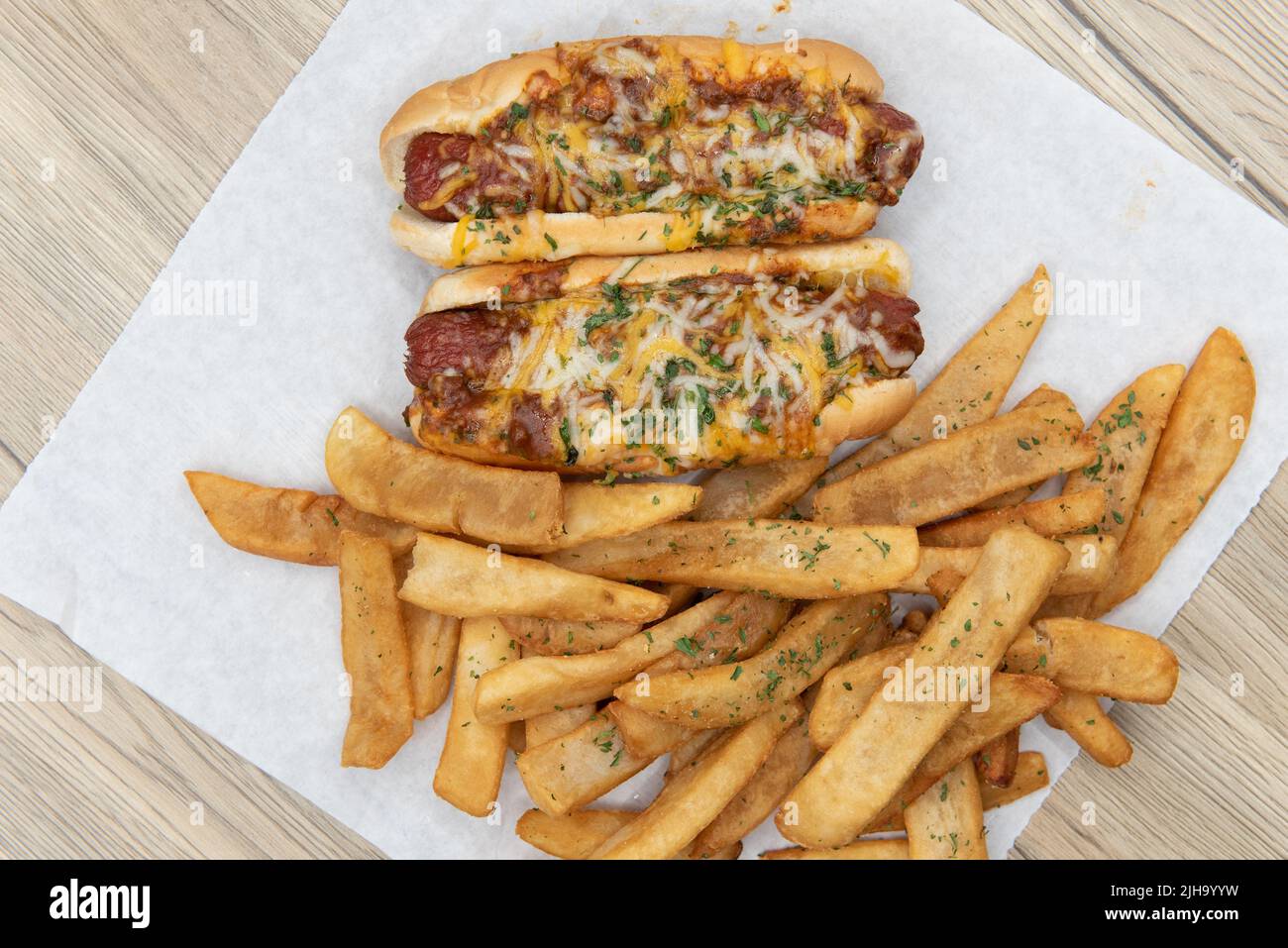 Vue en hauteur de deux hot dogs de chien au fromage Chili chargés de fromage fondu et servis avec des frites au steak de poivre pour un repas de faim d'appétit de fête. Banque D'Images