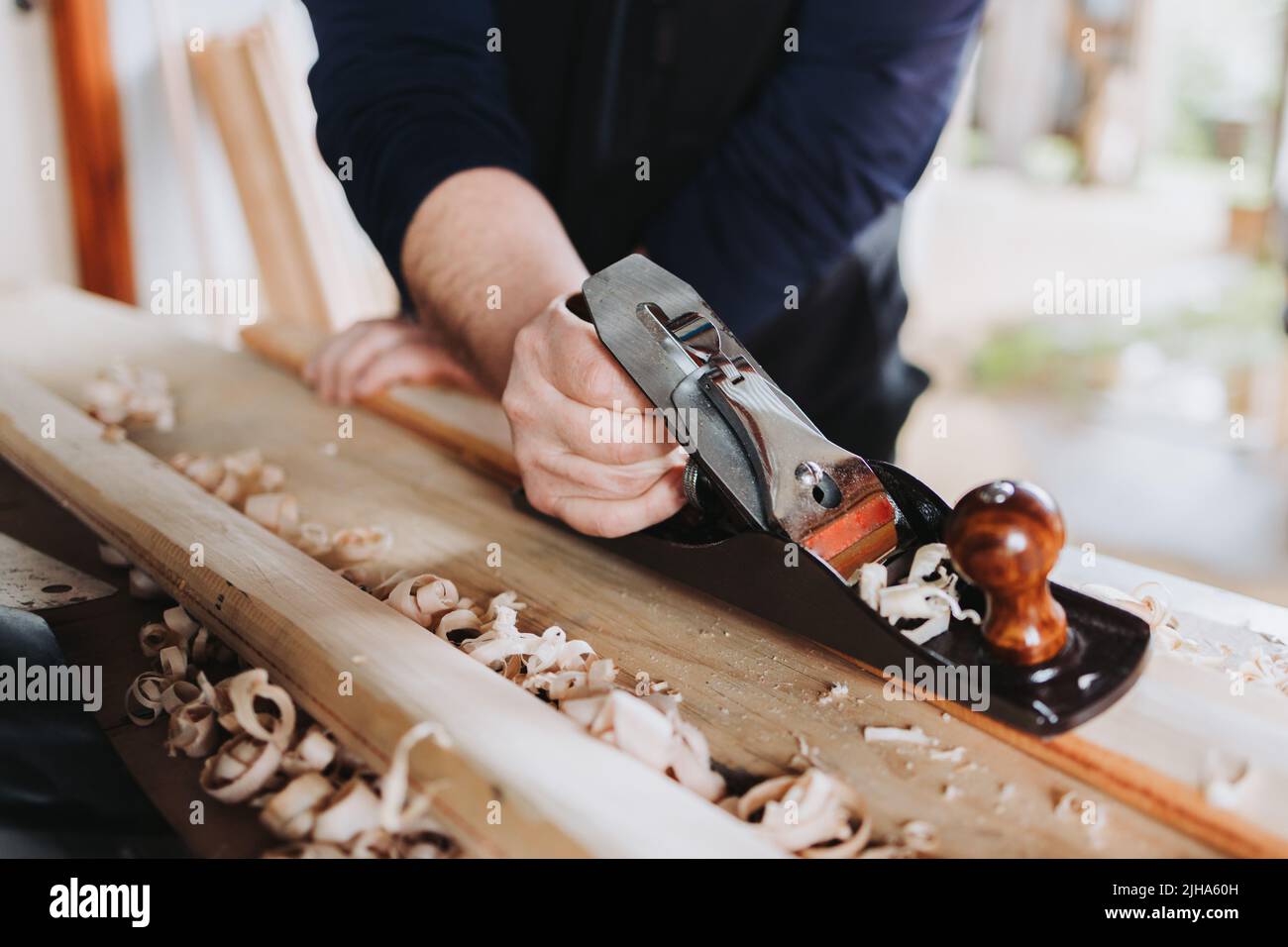homme méconnaissable utilisant une vieille brosse de charpentier en acier sculptant un bâton de bois, dans son atelier. Banque D'Images