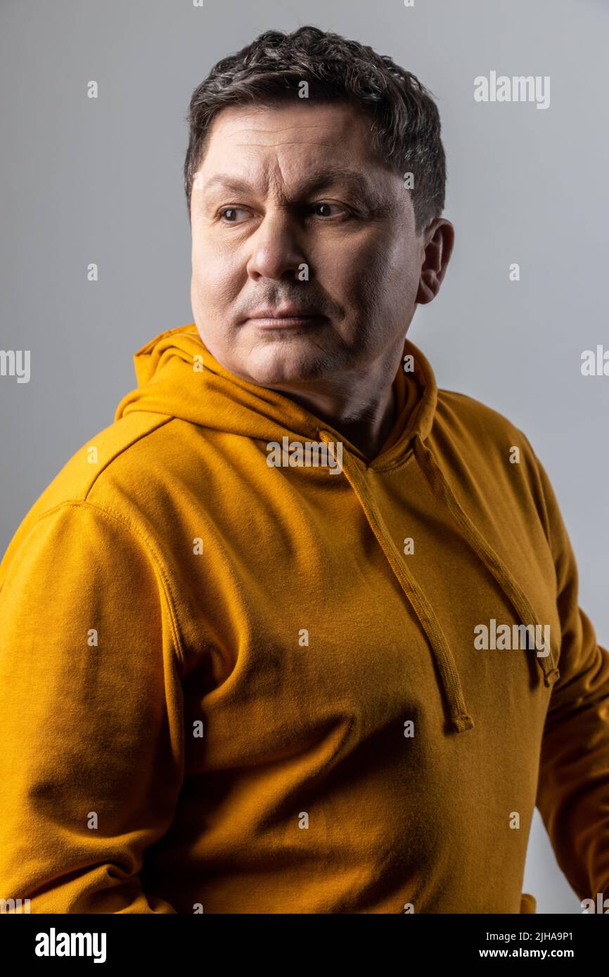 Portrait de beau pensif homme d'âge moyen regardant pensif, regardant loin, étant profondément dans les pensées, portant le sweat à capuche de style urbain. Prise de vue en studio isolée sur fond gris. Banque D'Images