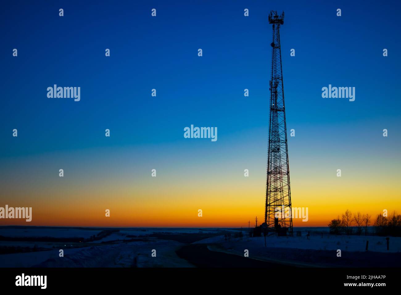 Vue nocturne d'une tour de télévision en métal sur une montagne au-dessus d'un village près d'une route d'automobile enneigée en hiver contre un ciel bleu foncé clair Banque D'Images
