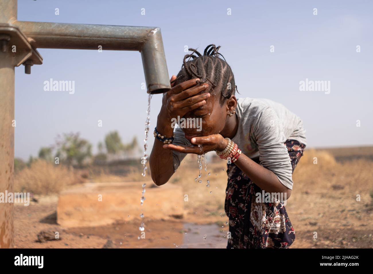 Petite fille africaine refroidissant son front et le visage sur une journée chaude brûlante au point d'eau du village Banque D'Images
