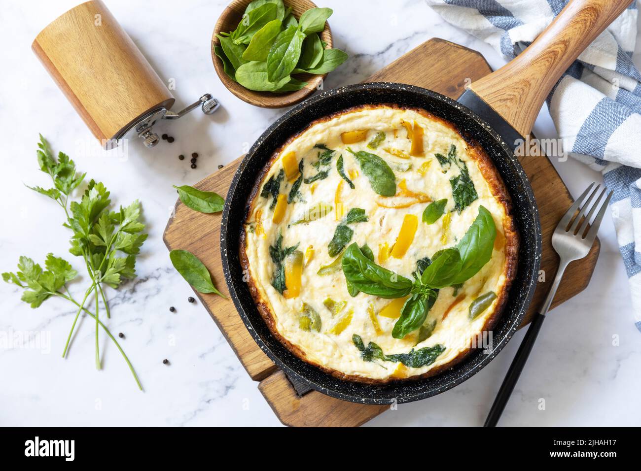 Omelette aux épinards et au fromage. Frittata fait d'oeufs, de paprika et d'épinards dans une poêle sur un comptoir en marbre. Vue de dessus. Banque D'Images