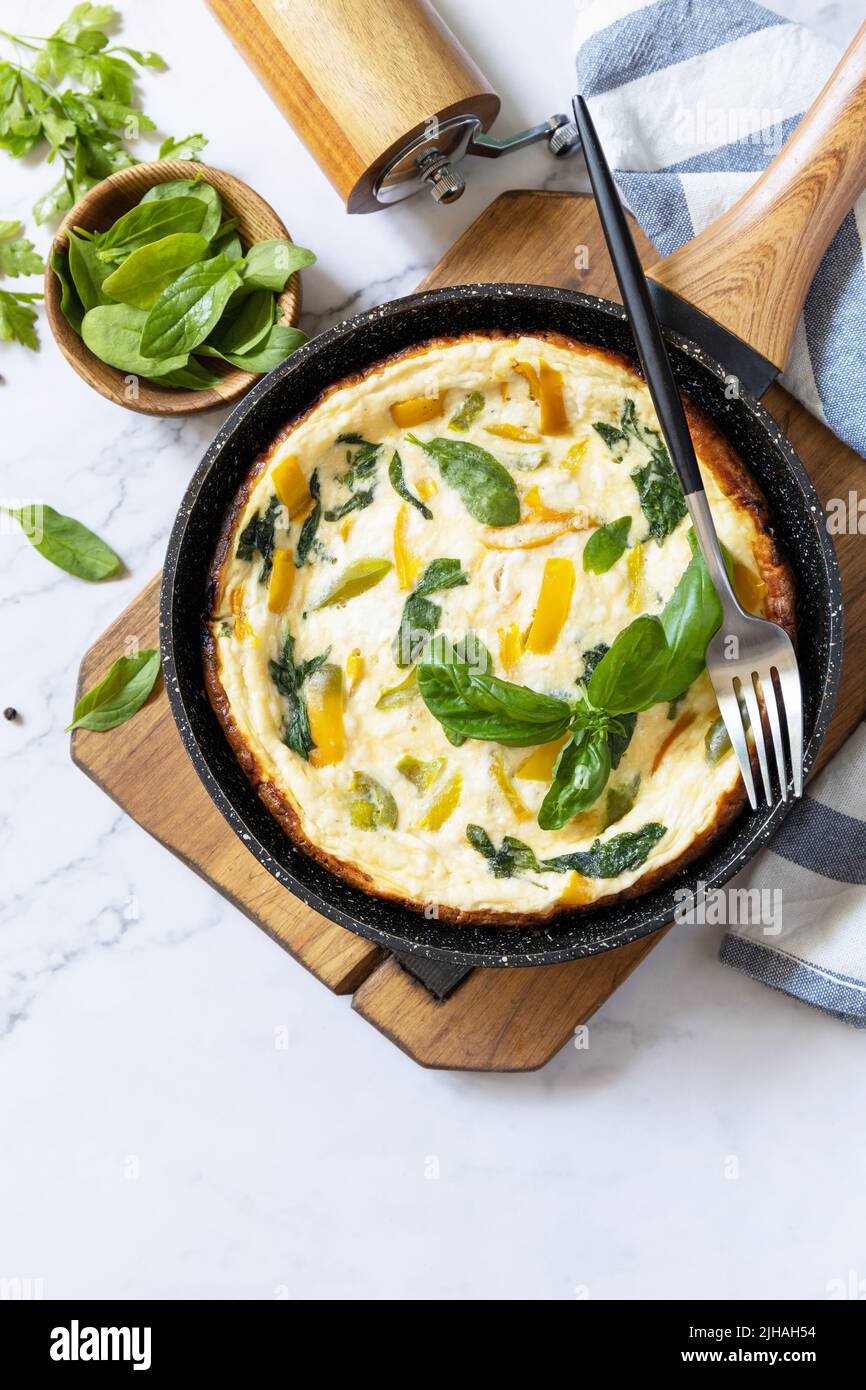Omelette aux épinards et au fromage. Frittata fait d'oeufs, de paprika et d'épinards dans une poêle sur un comptoir en marbre. Vue de dessus. Copier l'espace. Banque D'Images