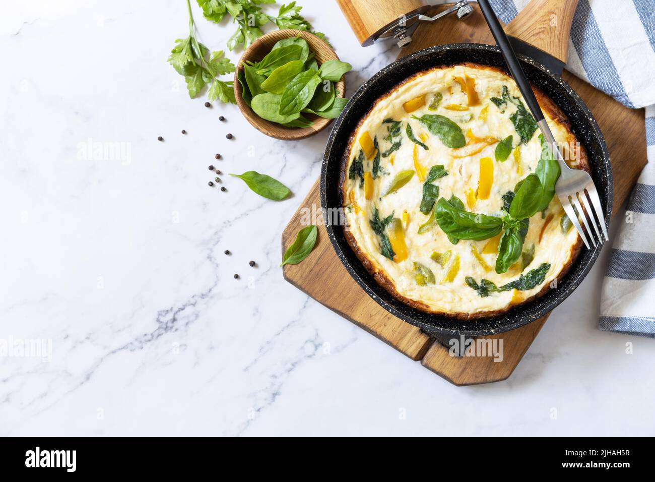 Omelette aux épinards et au fromage. Frittata fait d'oeufs, de paprika et d'épinards dans une poêle sur un comptoir en marbre. Vue de dessus. Copier l'espace. Banque D'Images