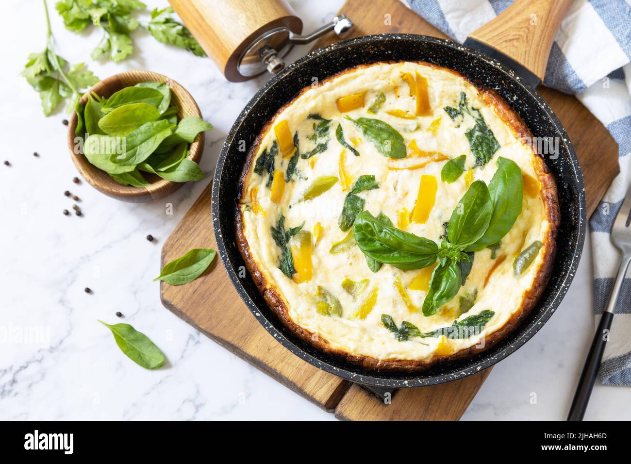 Omelette aux épinards et au fromage. Frittata fait d'oeufs, de paprika et d'épinards dans une poêle sur un comptoir en marbre. Copier l'espace. Banque D'Images