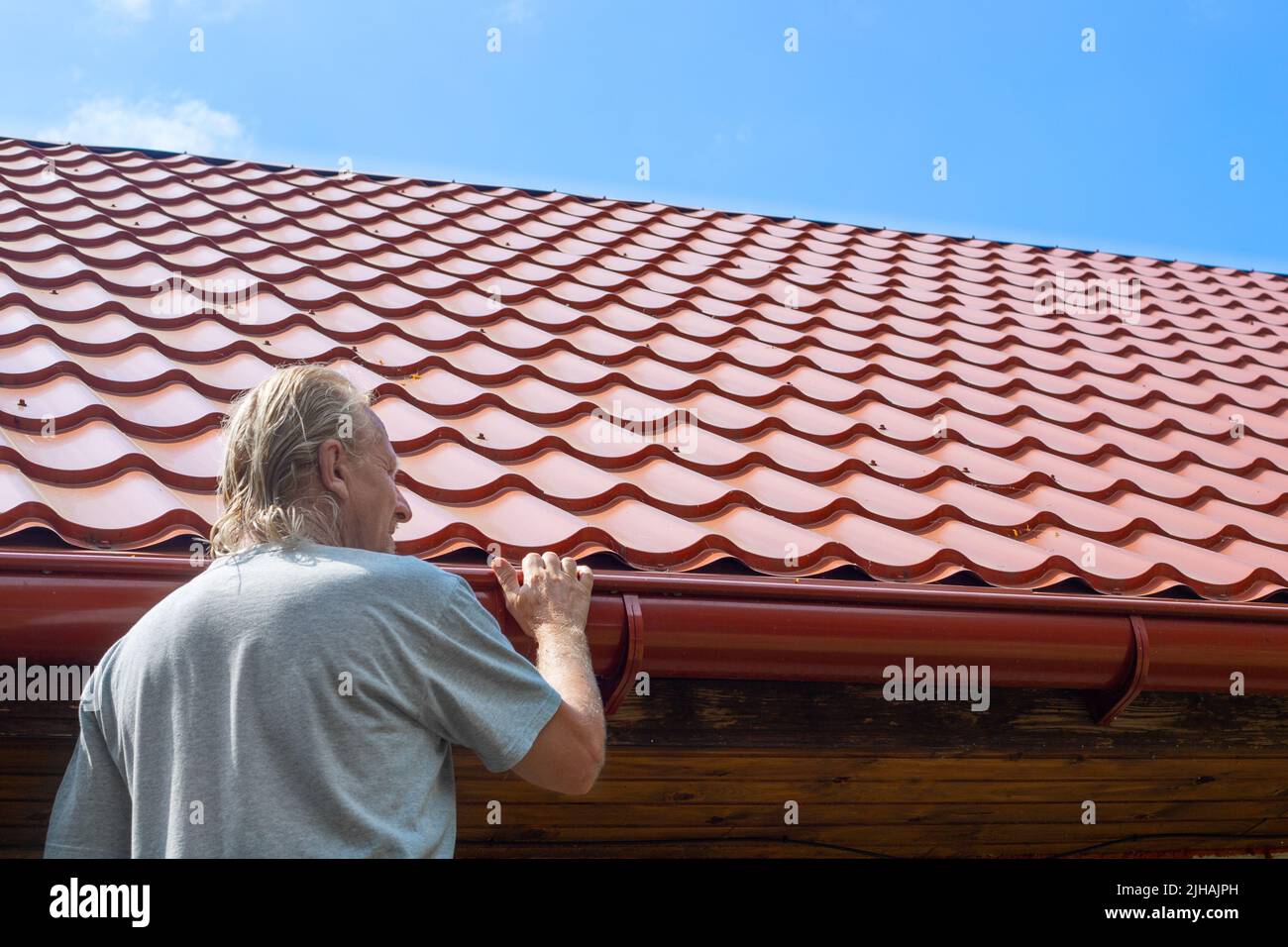 Un homme inspecte une gouttière sur un tuyau d'évacuation de toit. Drainage de l'eau de pluie du toit. Banque D'Images