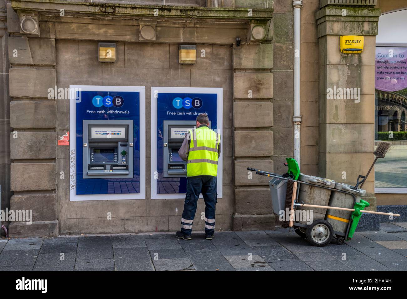 Un nettoyeur de rue utilisant un distributeur de billets TSB à Dundee. Banque D'Images