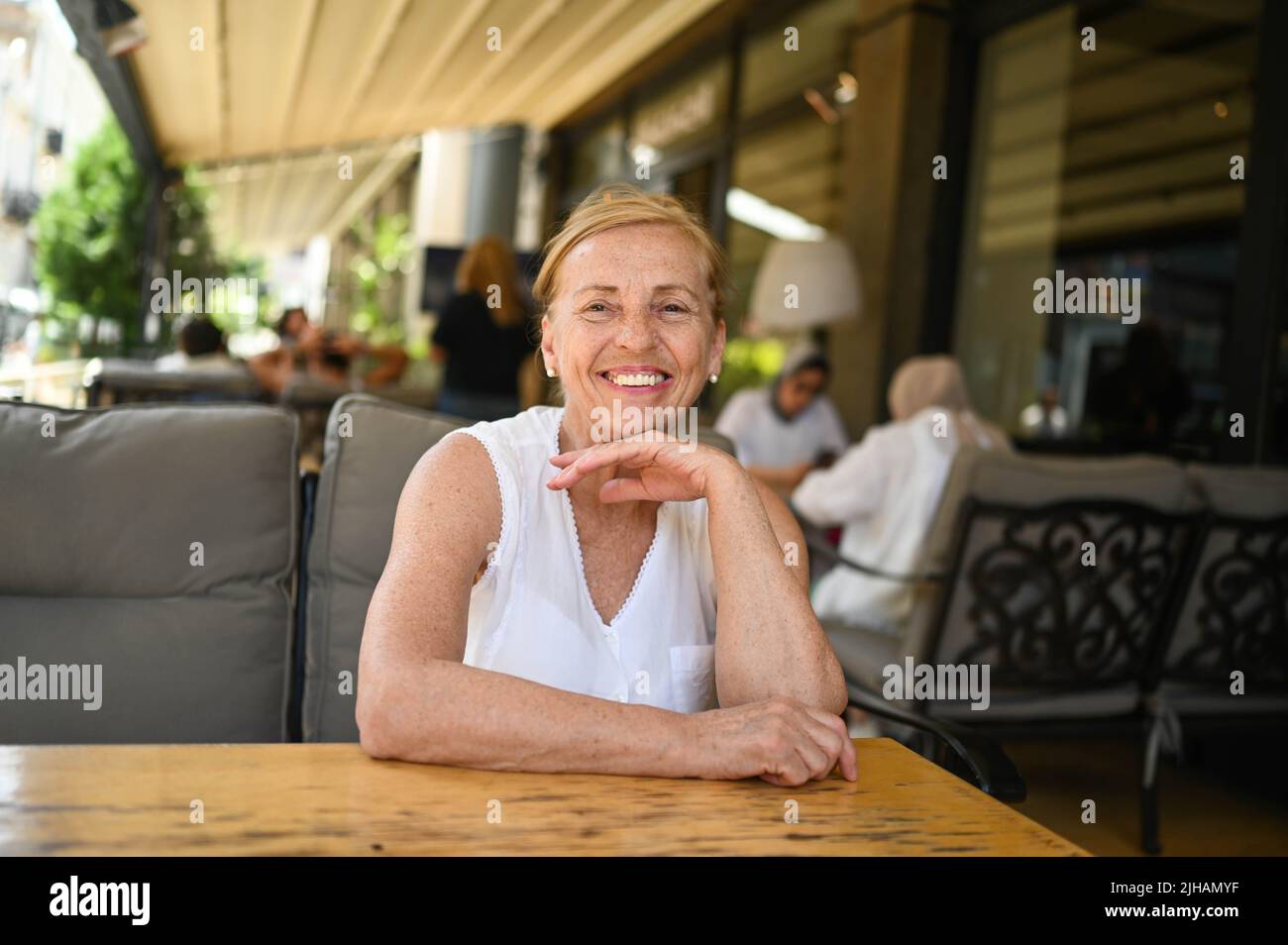 Bonne femme âgée avec un sourire parfait et des dents assis à l'extérieur, dans un café de rue ou sur la terrasse du restaurant. Retraite personnes matures vacances, concept de style de vie actif Banque D'Images
