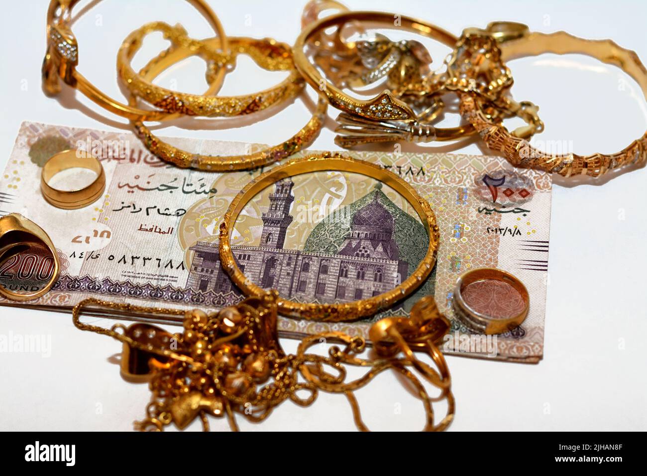 Une pile de billets d'argent en livres égyptiens avec un ensemble d'accessoires en or de bagues, chaînes de collier et bracelets isolés sur fond blanc, or v Banque D'Images
