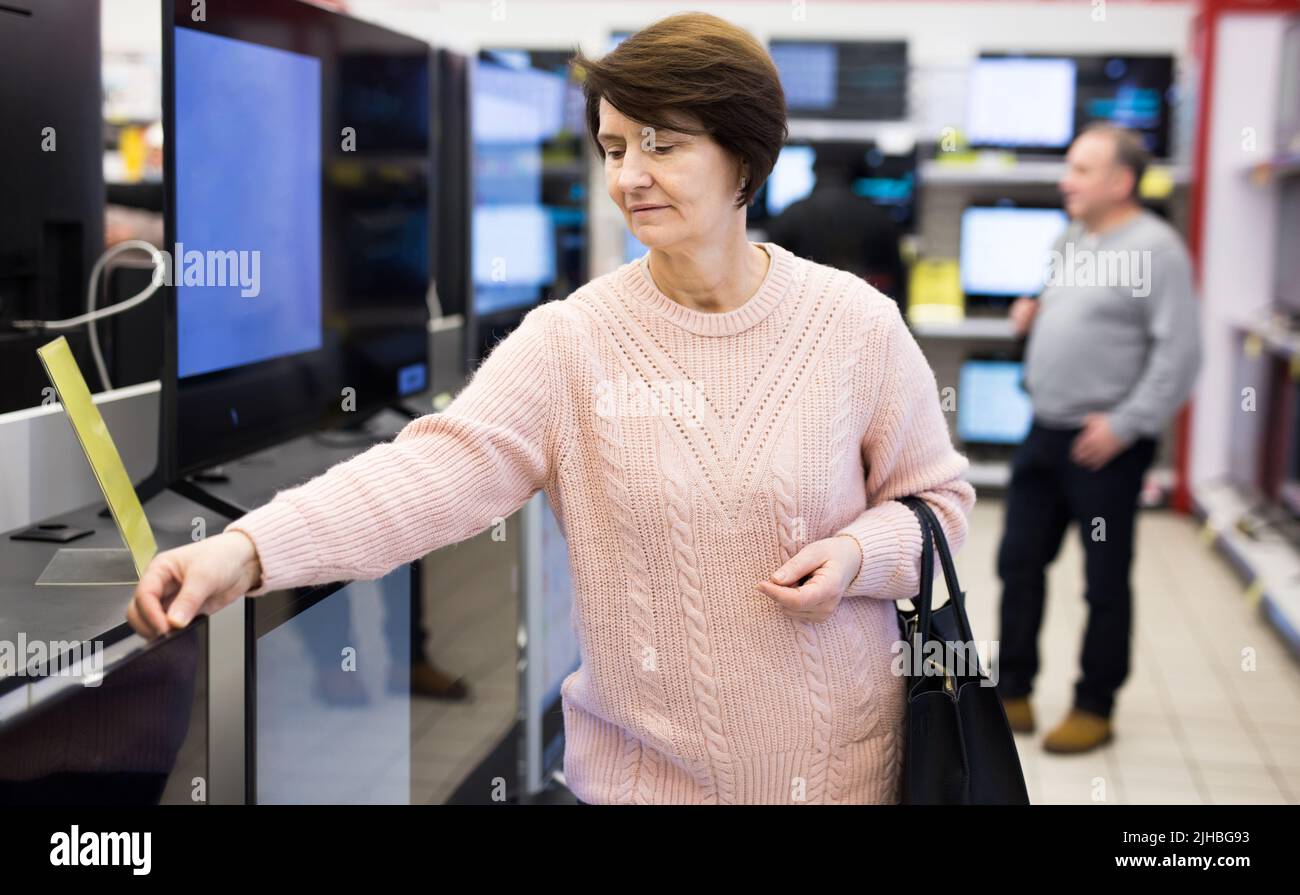 Femme d'âge mûr qui choisit la télévision dans un magasin d'électroménager Banque D'Images