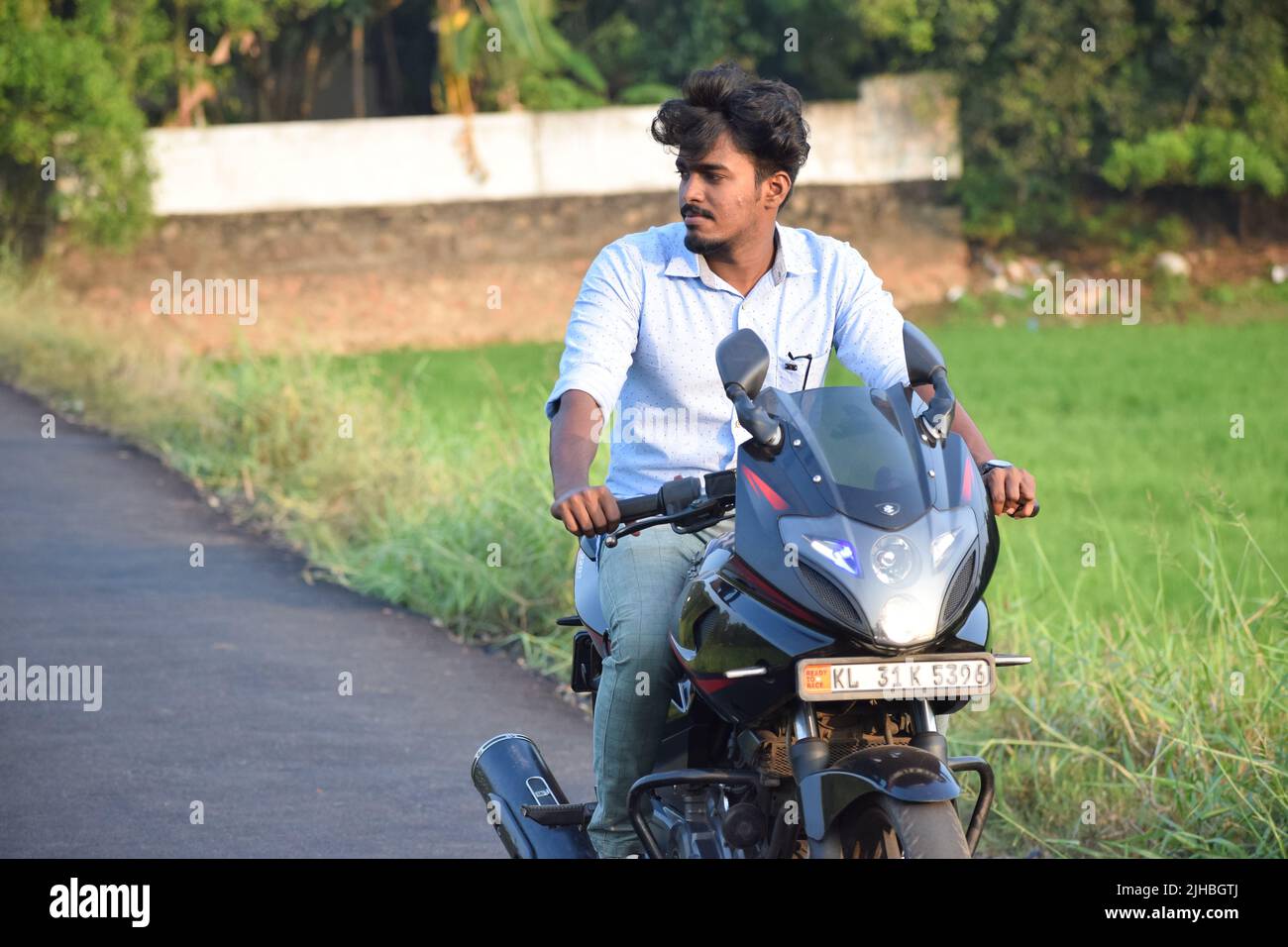 Un jeune indien qui fait une moto près d'un champ de paddy Banque D'Images