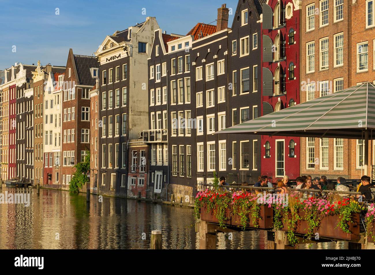 Dîner sur le Damrak, Amsterdam au coucher du soleil, surplombant l'eau avec des maisons hollandaises en bord de canalside en arrière-plan Banque D'Images
