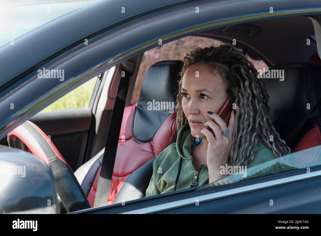 Portrait d'une femme asiatique d'âge moyen attrayante, parlant au téléphone, dans une fenêtre de voiture ouverte. Banque D'Images