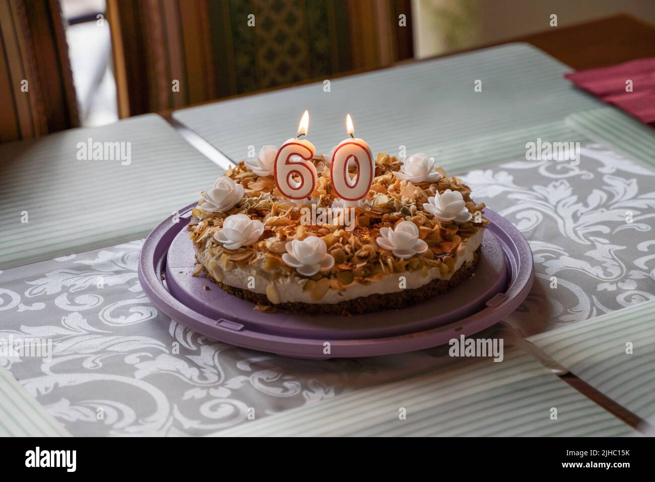 Gros plan d'un gâteau d'anniversaire avec bougie en feu 60 ans anniversaire sur la table pour la célébration. Délicieux gâteau fait maison avec roses blanches et pistaches Banque D'Images
