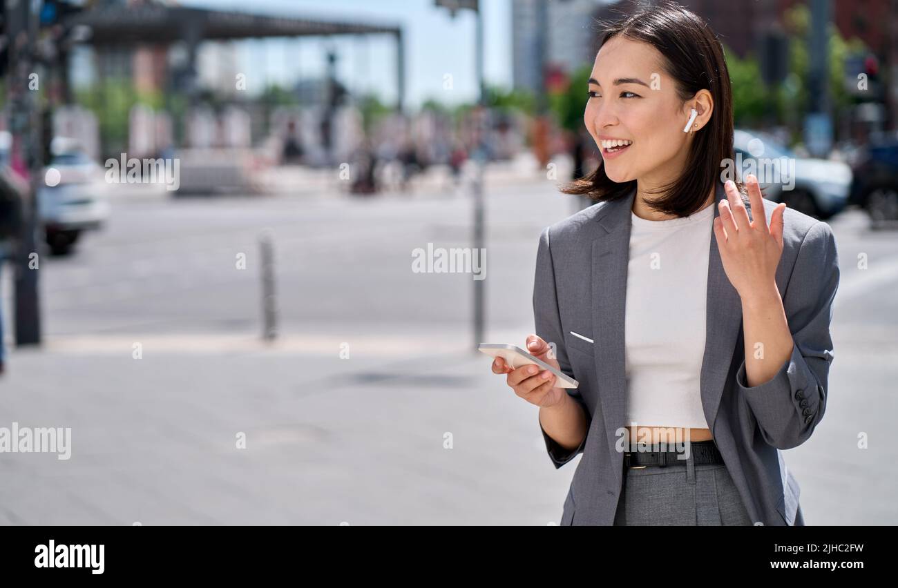 Jeune femme asiatique parlant au téléphone avec des écouteurs sans fil dans la rue de la ville. Banque D'Images