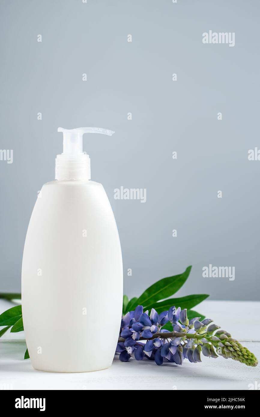 Bouteille cosmétique avec lotion et fleurs lupin sur fond gris. Cosmétiques naturels pour les soins du corps et du visage. Concept de produits spa bio, relaxati Banque D'Images