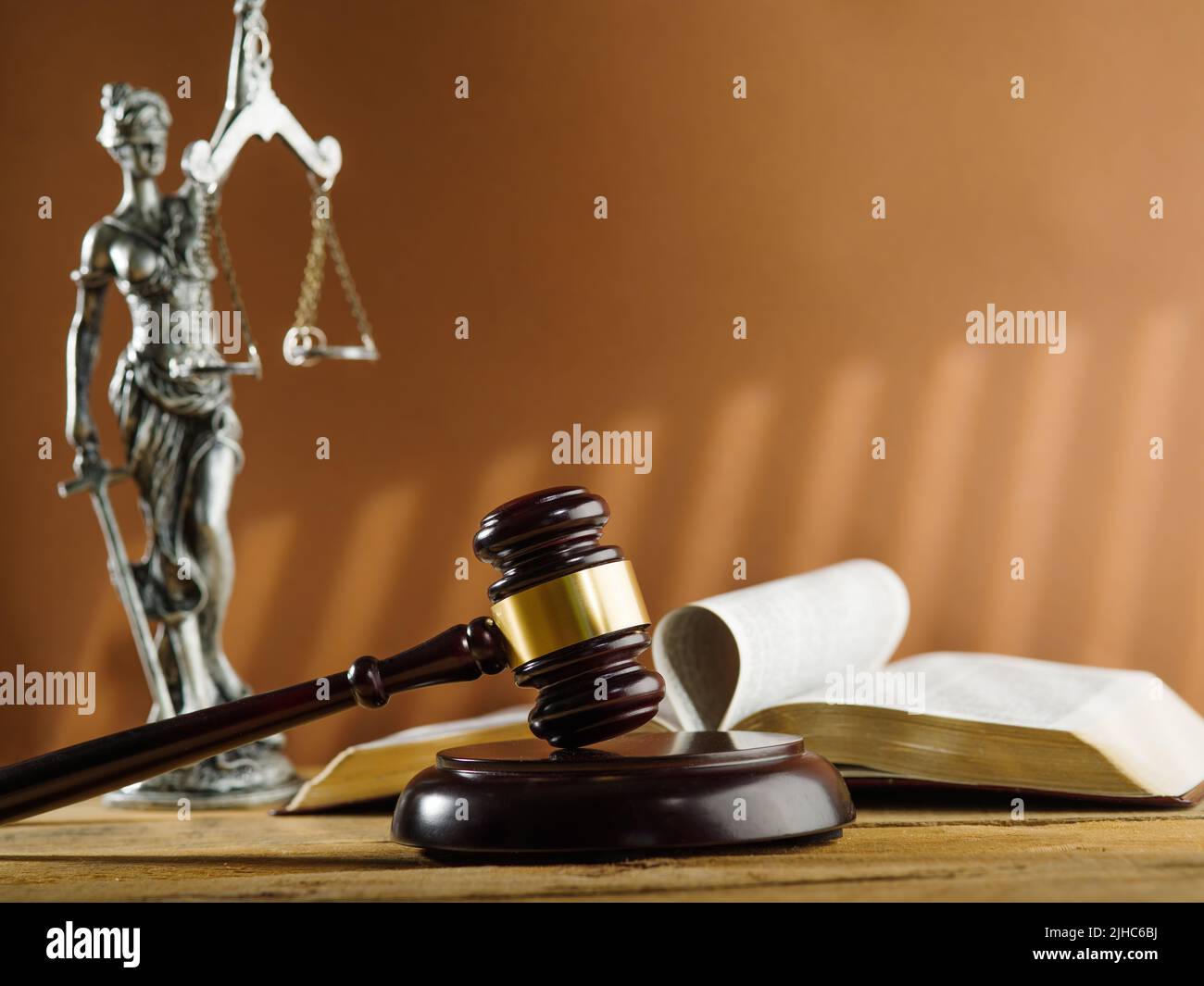 Jugement et justice. Un gavel du juge, un livre ouvert et une statue en bronze de la déesse de la justice - Themis sur fond beige foncé. Banque D'Images