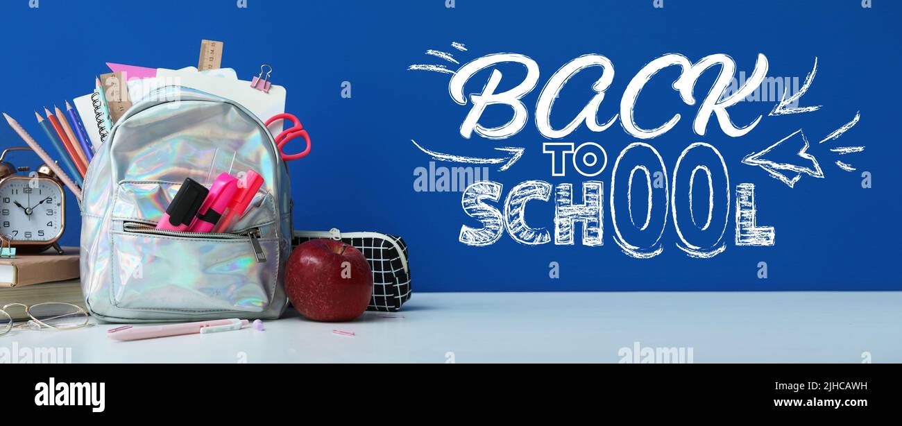 Sac à dos avec papeterie, horloge et pomme sur table sur fond bleu. Retour à l'école Banque D'Images