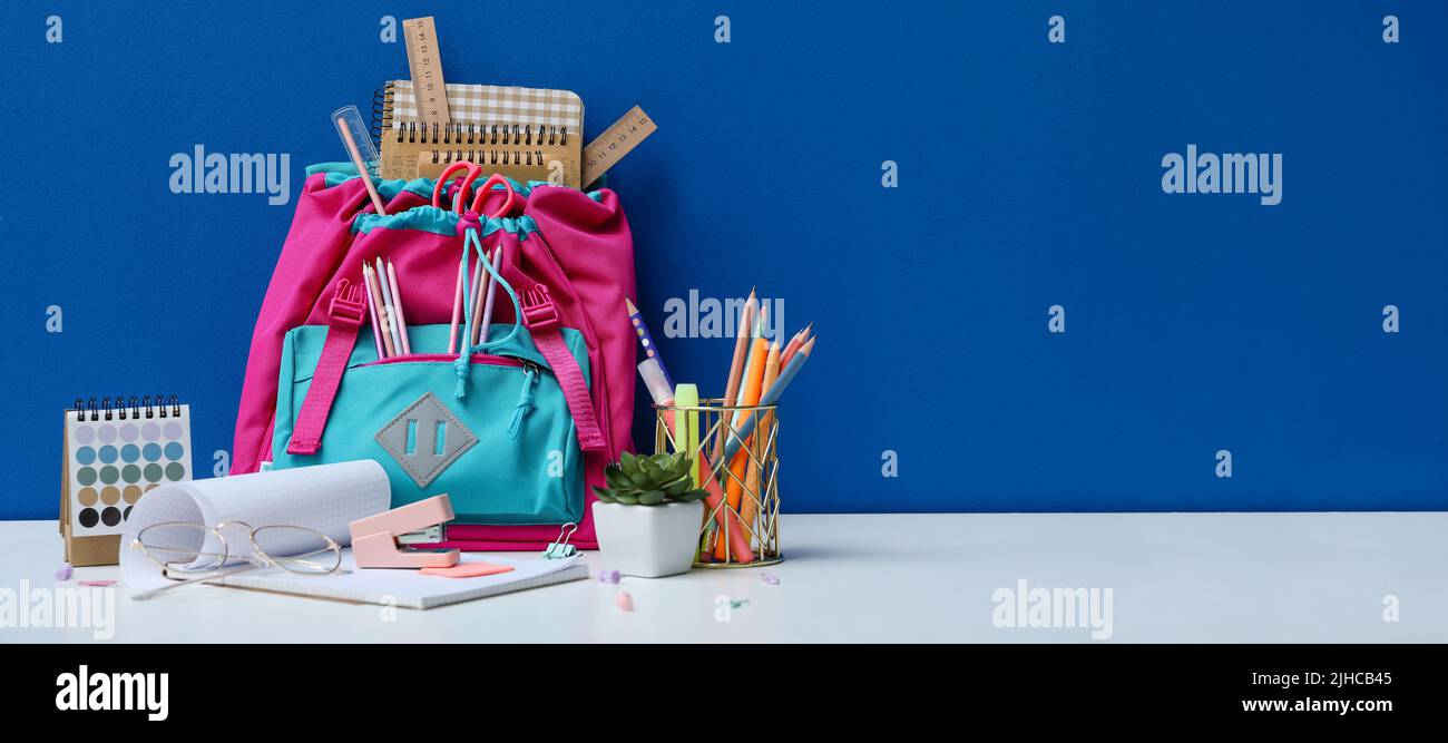 Sac à dos pour l'école avec papeterie sur table sur fond bleu Banque D'Images