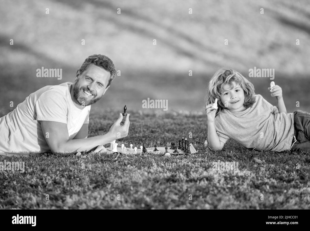 famille heureuse de père homme et fils enfant jouant aux échecs sur l'herbe verte dans le parc extérieur, amitié Banque D'Images