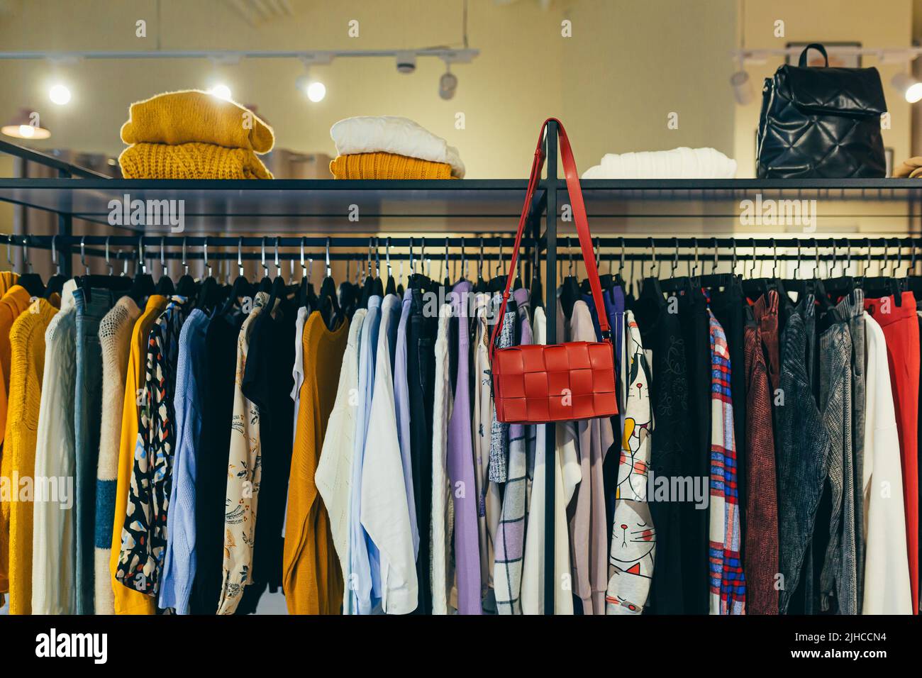 Magasin de mode. Plusieurs vêtements de style professionnel pour femmes accrochés sur une étagère dans la salle d'exposition. Sucettes, chapeau, accessoires Banque D'Images
