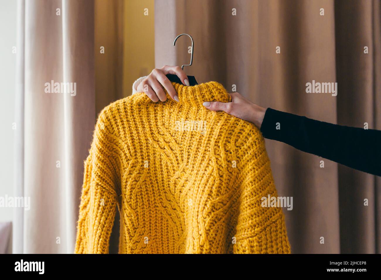 Gros plan. La main d'un vendeur ou d'un consultant passant des vêtements, un chandail jaune sur un cintre, à la main d'un client qui attend dans la cabine d'essayage derrière les rideaux. Dans un magasin de vêtements dans un centre commercial Banque D'Images