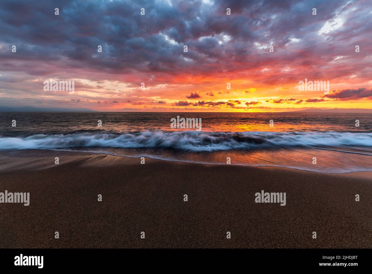 Une vague d'océan se brise sur Une plage tropicale contre Un ciel de coucher de soleil coloré Banque D'Images