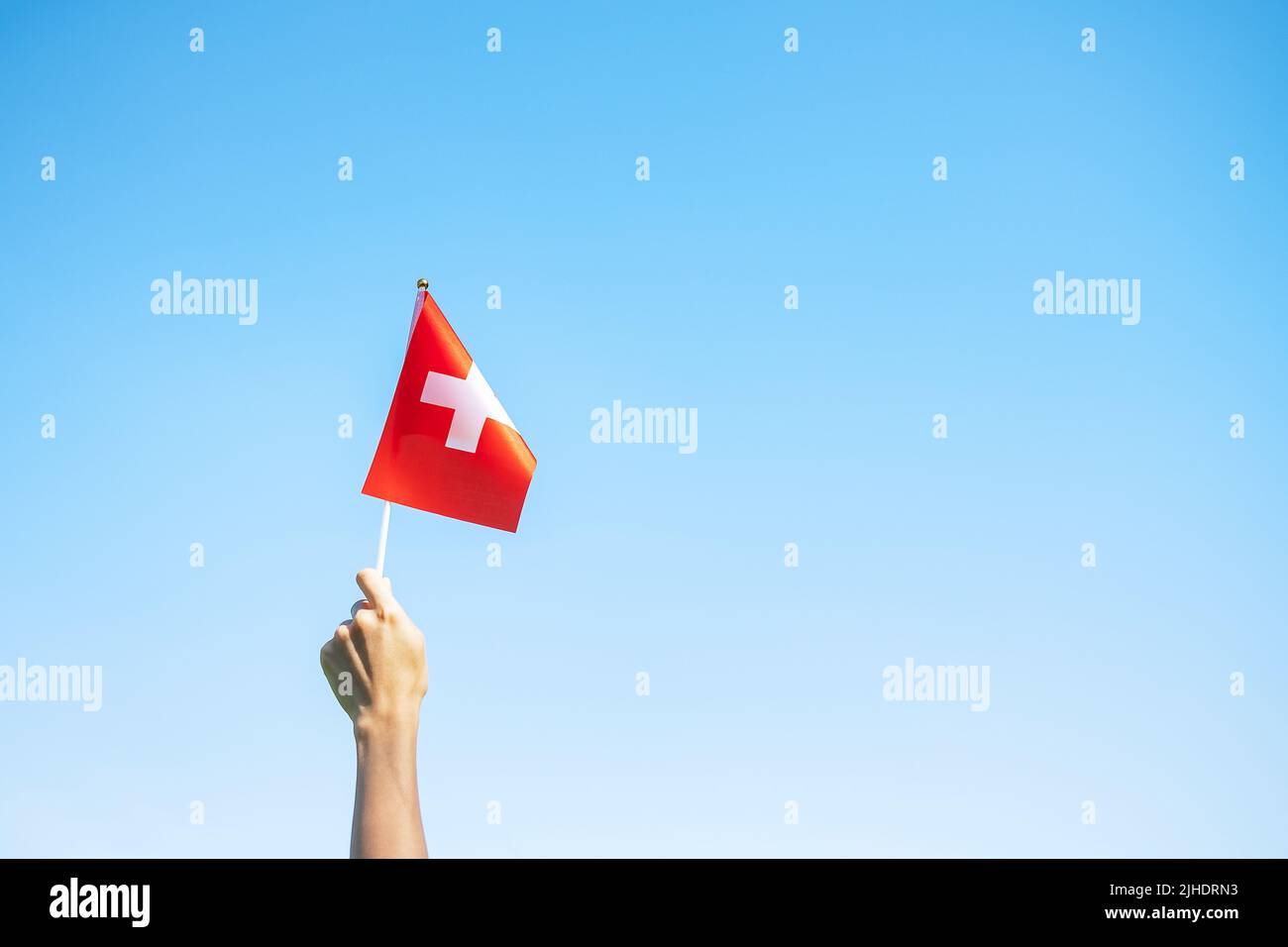 Main tenant le drapeau suisse sur fond bleu ciel. Concepts de la Journée nationale de la Suisse et de la célébration heureuse Banque D'Images