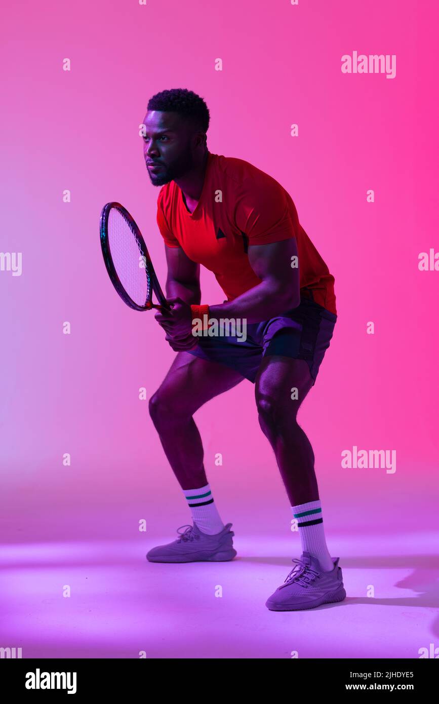 Image verticale d'un joueur de tennis afro-américain dans un éclairage rose fluo Banque D'Images