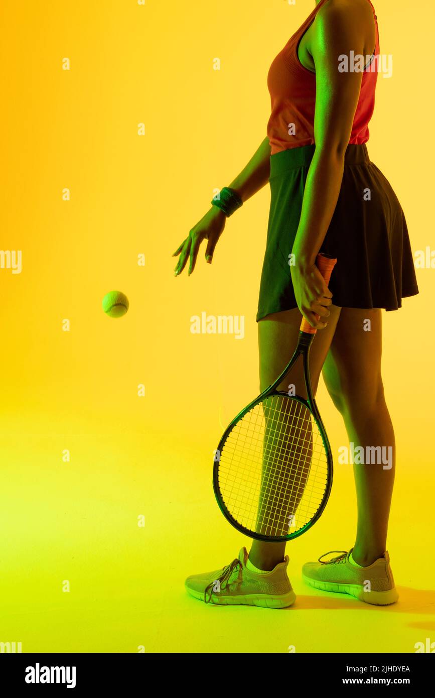 Image verticale de la section médiane d'une joueuse de tennis afro-américaine dans un éclairage jaune Banque D'Images