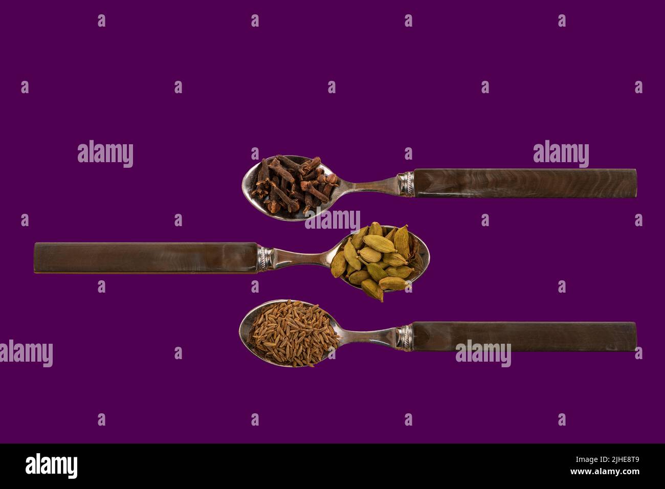sélection assortiment d'épices indiennes graines de cumin cardamome gousses cardamon clous de girofle exposés sur des cuillères sur un fond violet coloré Banque D'Images