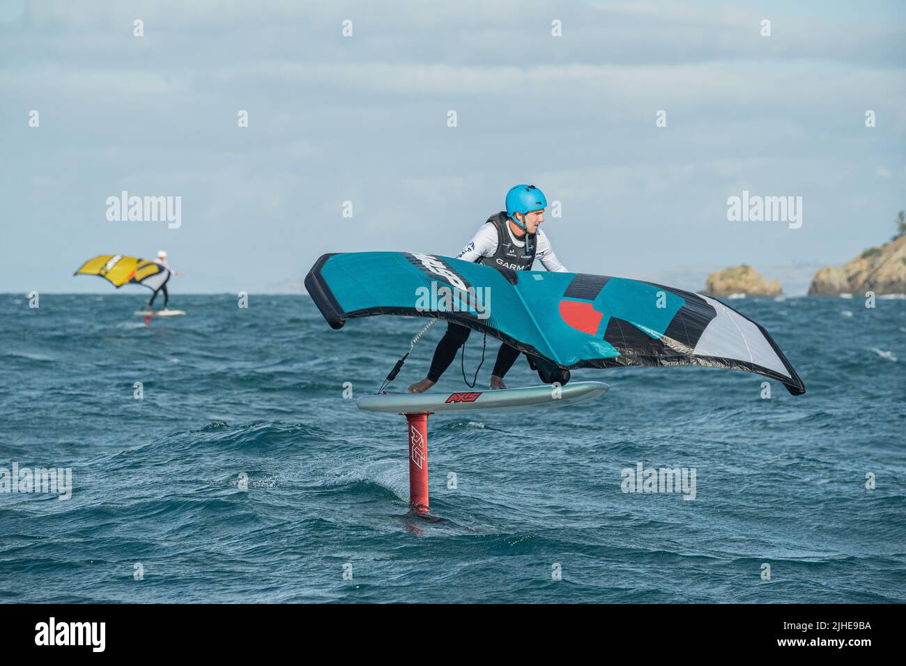 Une aile d'homme fait des feuilles en mer à l'aide d'une aile gonflable à la main, à cheval sur une planche de surf. Baie d'Hauraki, Auckland, Nouvelle-Zélande. Banque D'Images