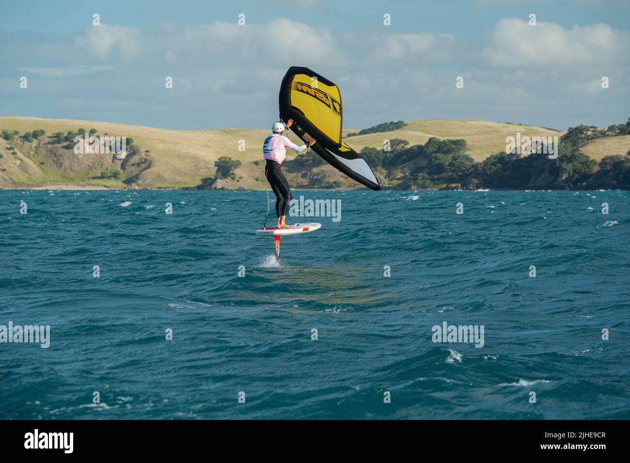 Une aile d'homme fait des feuilles en mer à l'aide d'une aile gonflable à la main, à bord d'une planche à voile hydrofoil. Baie d'Hauraki, Auckland, Nouvelle-Zélande. Banque D'Images
