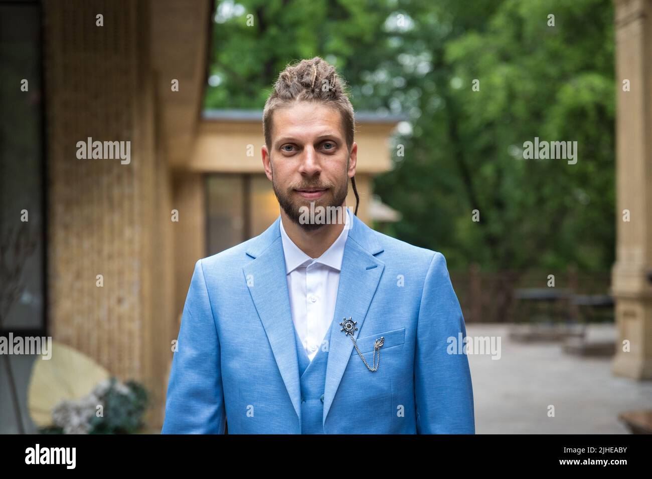 Portrait d'un jeune homme de 25 ans avec une coiffure hippster et une barbe en costume bleu trois pièces dans un espace de restaurant dans un parc Banque D'Images