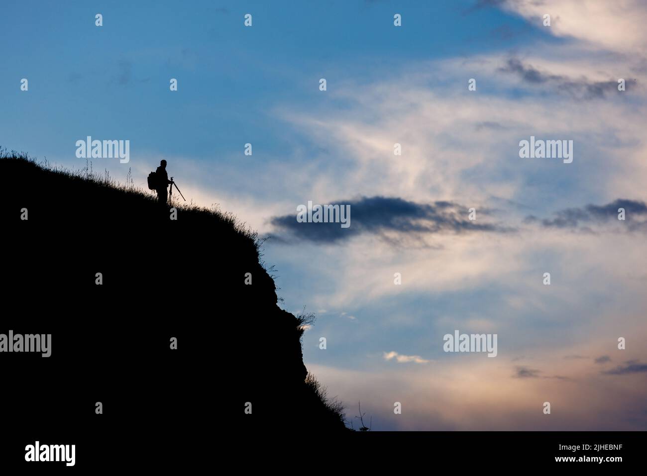 silhouette de photographe avec trépied sur la falaise avec ciel bleu nocturne avec fond de nuages Banque D'Images