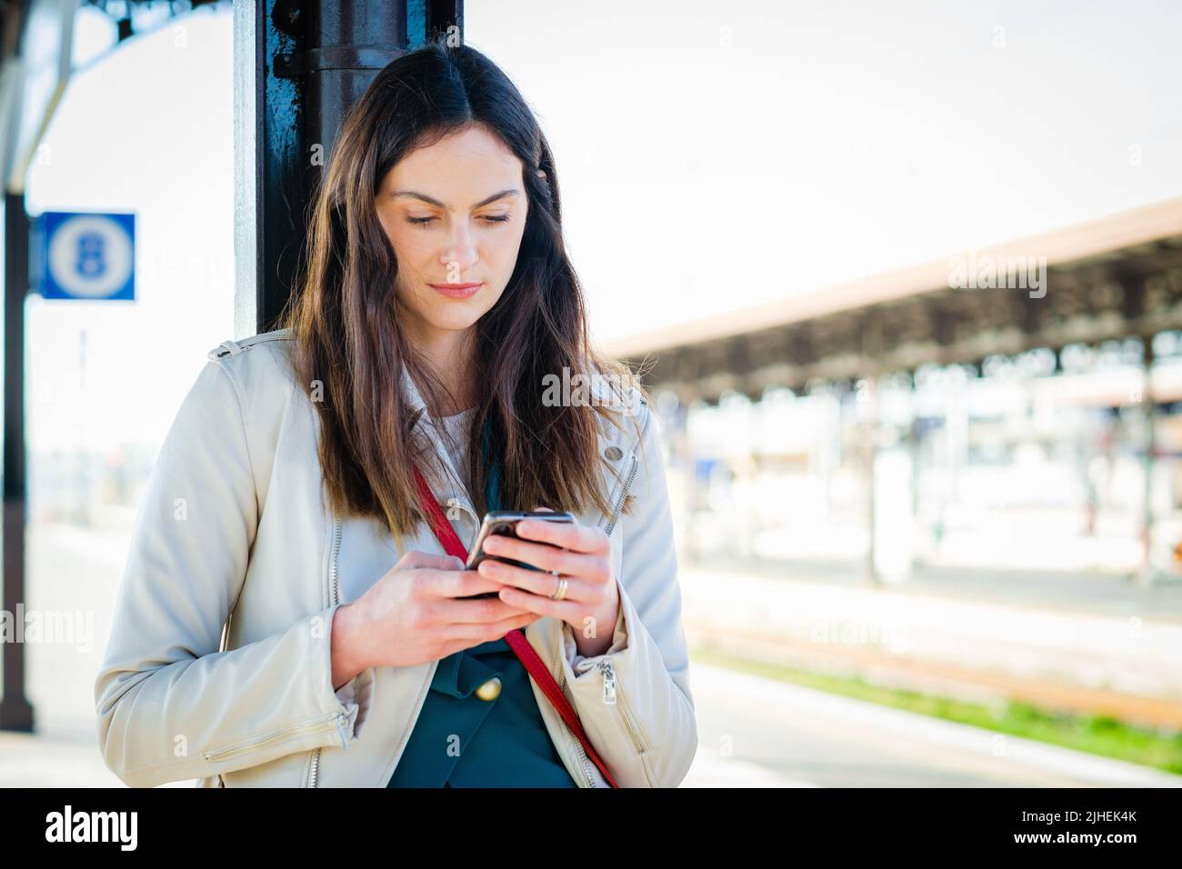 Femme d'affaires souriante utilisant un smartphone en attendant dans une gare - jeune fille étudiante attrayante utilisant le téléphone portable en position debout Banque D'Images