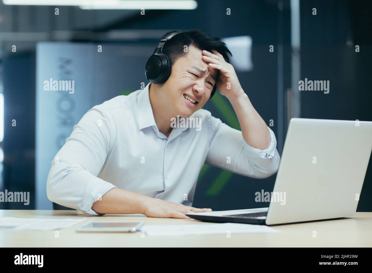 Homme d'affaires asiatique regardant un match de sport au bureau, homme regardant déçu par l'ordinateur portable, utilisant des écouteurs pour écouter Banque D'Images